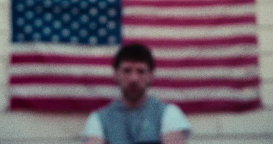 The blurred image focuses on a man sitting before a flag