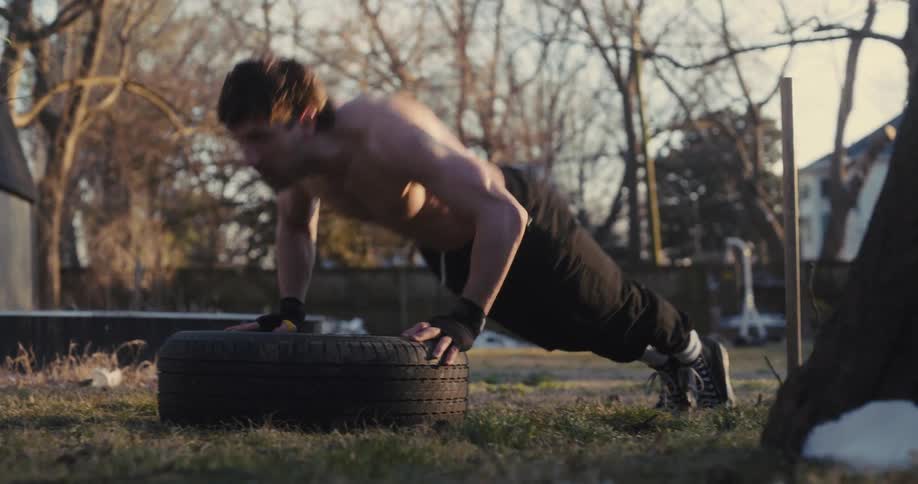 Man performs pushups supported on a tire outdoors
