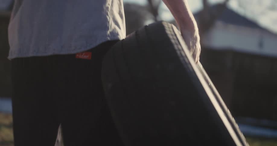 Man holds a car tire with one hand outdoors