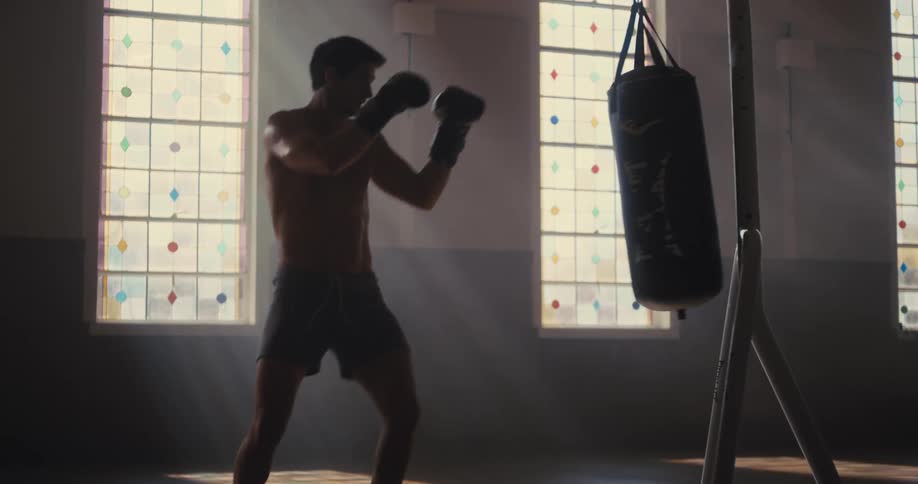 Man practices boxing on a punching bag in front of stained glass windows