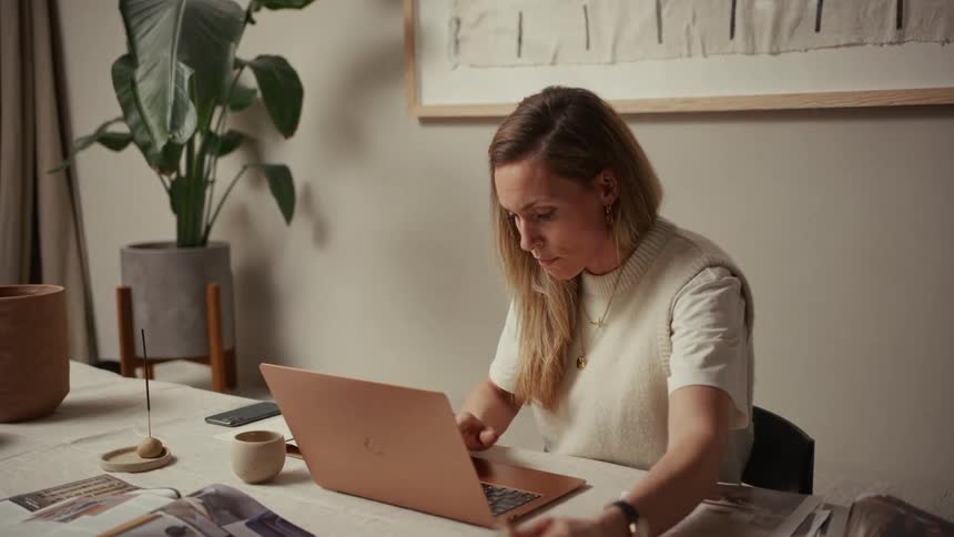 Woman works on a laptop at a table with magazines and fabric samples