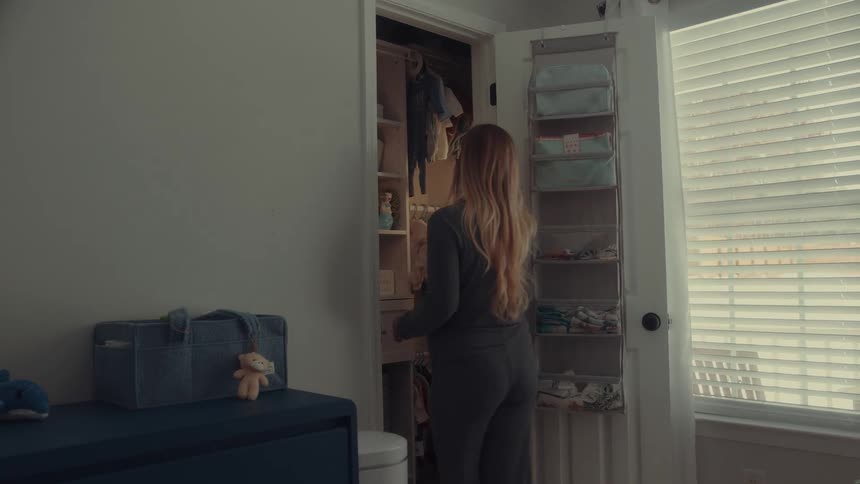 Woman arranges baby clothes in closet lit by natural light