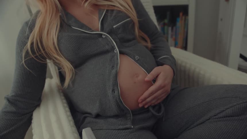 Pregnant woman sitting while holding a mug and resting her hand on her belly
