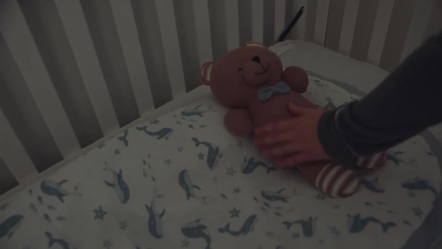 Female places a teddy bear in a crib and strokes its fur