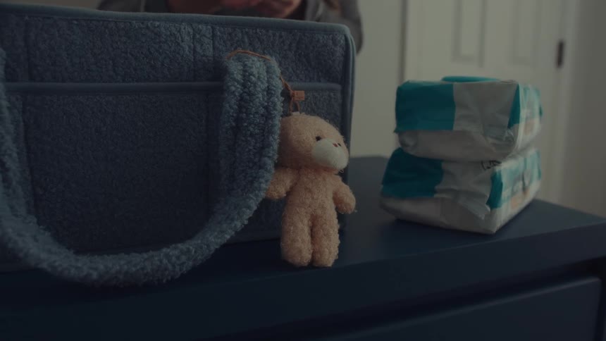 A close view of a blue storage caddy on a dresser shows a small plush bear keychain attached to the handle as a person organizes items inside it