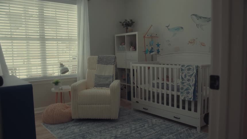 A cozy nursery features a white crib and a creamcolored rocking chair set against walls decorated with blue whale decalsnatural light filters through horizontal blinds and white curtains illuminating a soft blue patterned rug on the floor