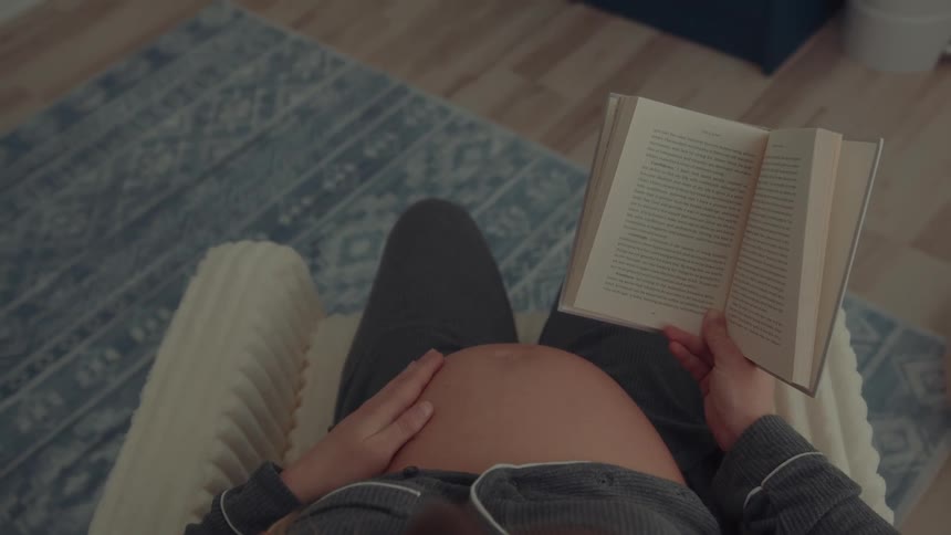 Pregnant person reading book in cozy setting