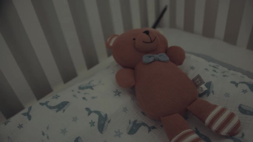 Woman places a teddy bear into an empty crib