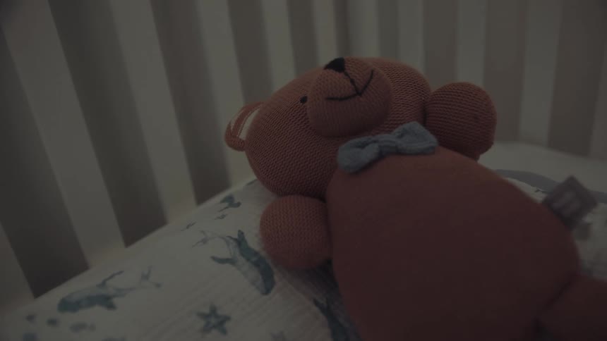 Knitted teddy bear with a blue bow is placed on a nauticalthemed blanket in a crib
