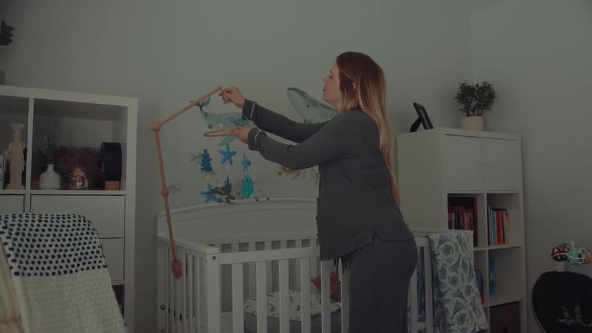 Pregnant woman attaches a hanging mobile above a babys crib in a nursery