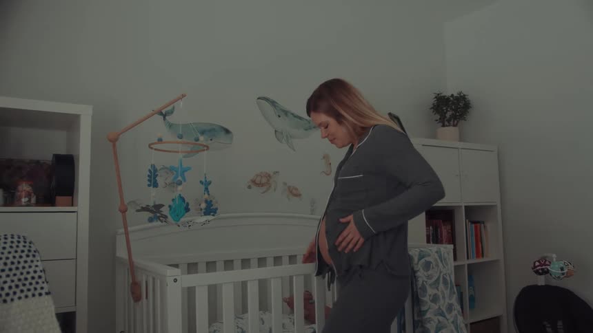 Woman interacts with oceanthemed mobile above crib in nursery