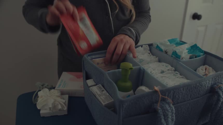 A pregnant woman organizing her supplies into a basket indoors