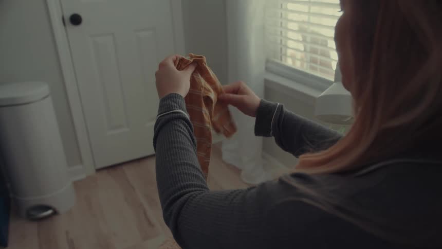 Expectant mother folds baby clothes while sitting indoors