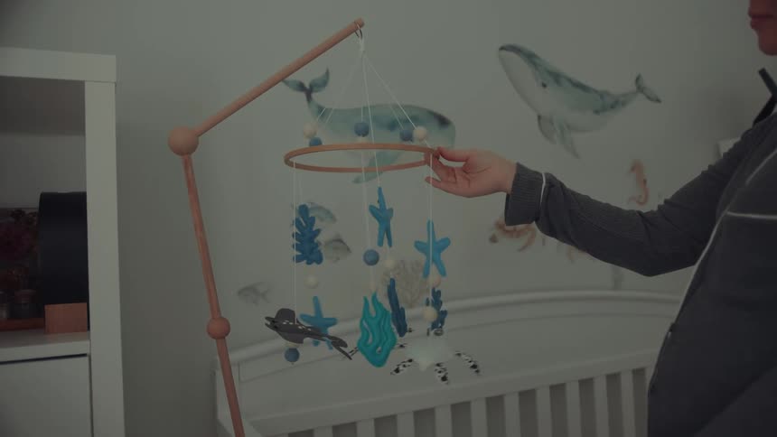 Person holds oceanthemed mobile above crib in nursery decorated with marine motif