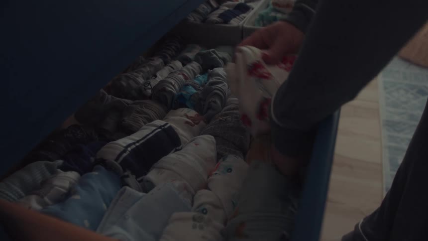Drawer with organized baby clothes being arranged by adult hands
