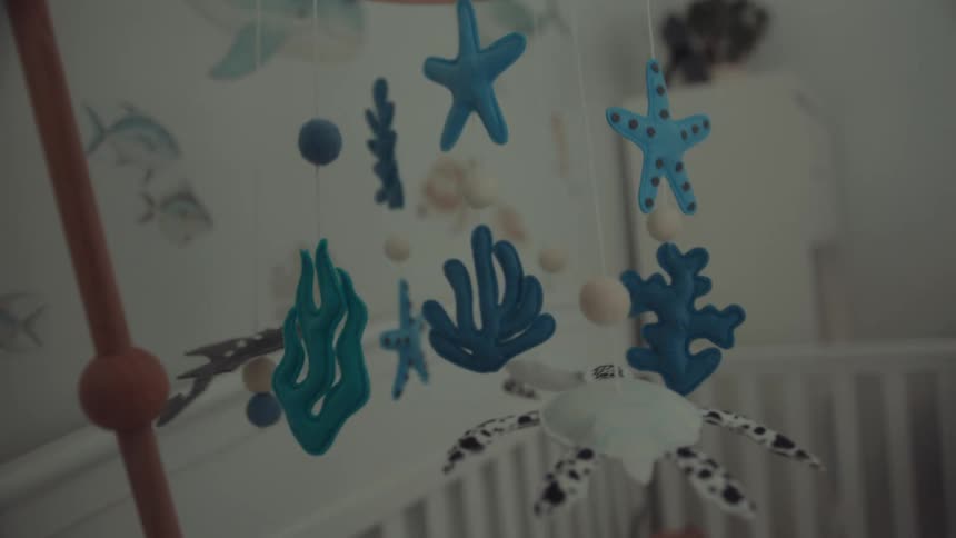 A persons hand spinning an oceanthemed baby mobile hanging above a crib indoors at midday