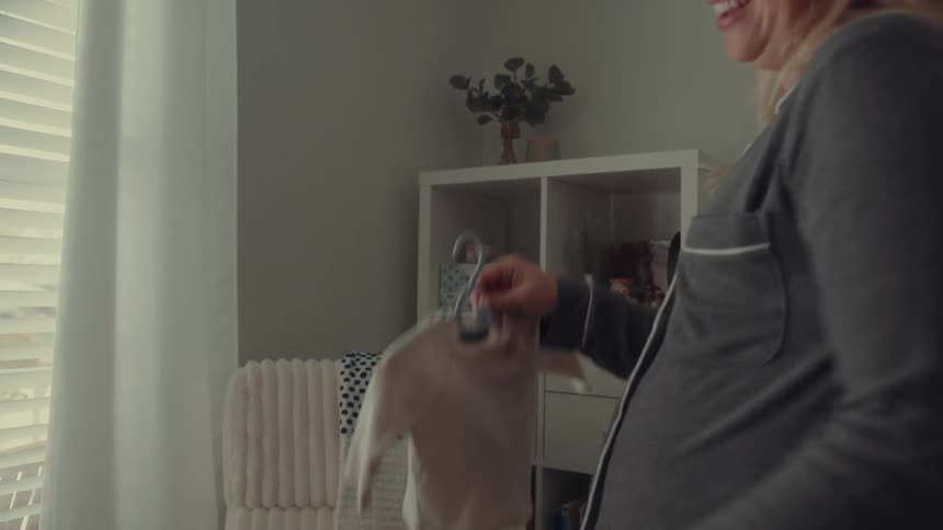 Pregnant woman organizes baby clothes in lit closet