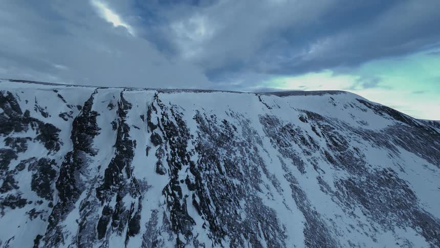 Snowcovered mountain ridge with rocky slopes under partly cloudy sky