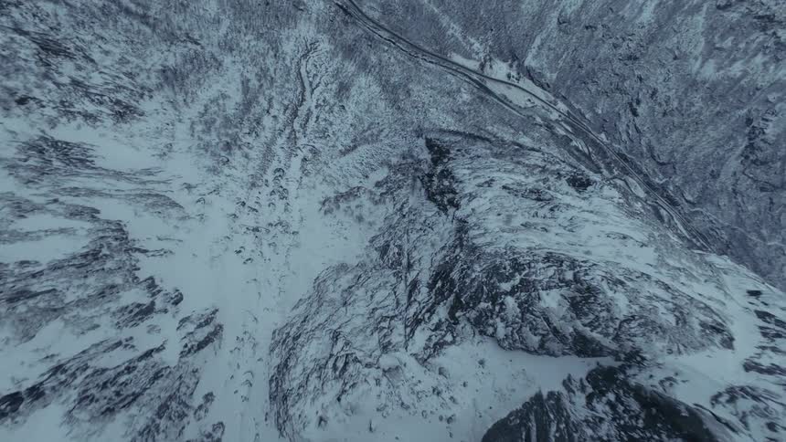 A dark winding asphalt road snakes through the valley floor it provides a sharp color contrast against the surrounding white snow and gray rock following the natural curve of the mountain base