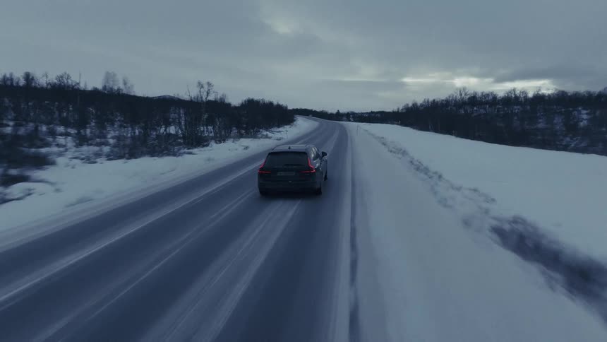 Black car drives along snowcovered road in winter landscape
