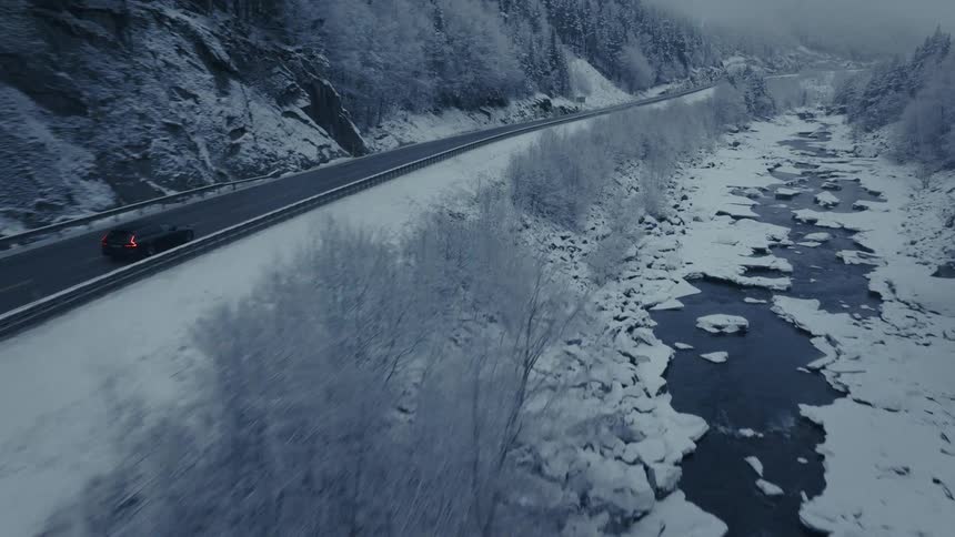 A solid yellow line runs along the left side of the lane separating the driving path from the mountainside shouldera solid white line runs along the right side of the road marking the edge closest to the snowcovered embankment and the river