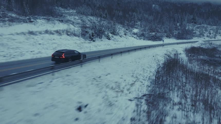 A sport sedan driving on a countryside freeway on a winter day with snow covering both sides of the road