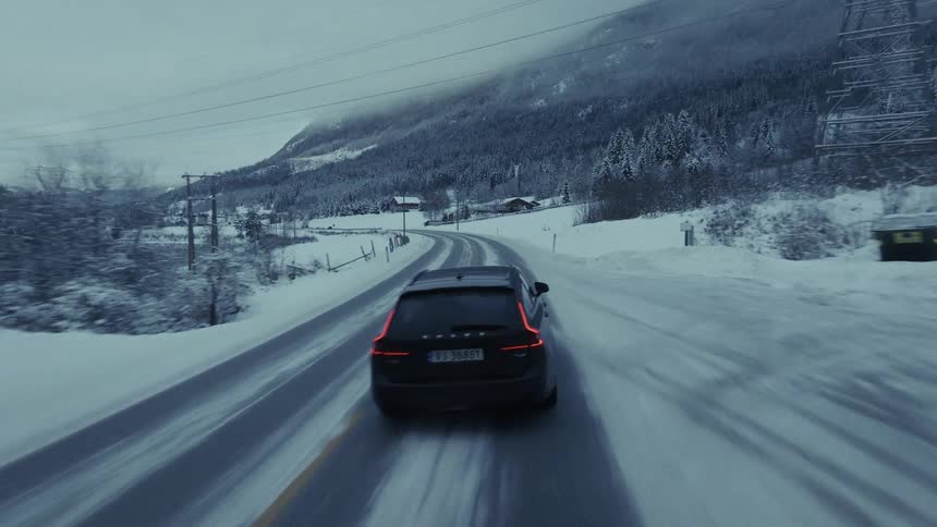 Van traveling on a forested mountain road along the coast of a frozen river valley