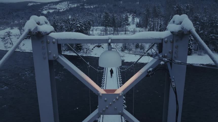 Man walks across a snow covered bridge to the forest