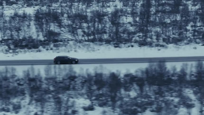 Black car drives along clear road in snowy landscape