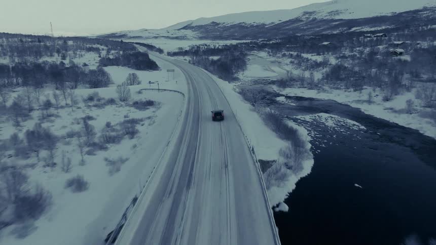 Automobile travels on a snow covered freeway through woodland and mountains