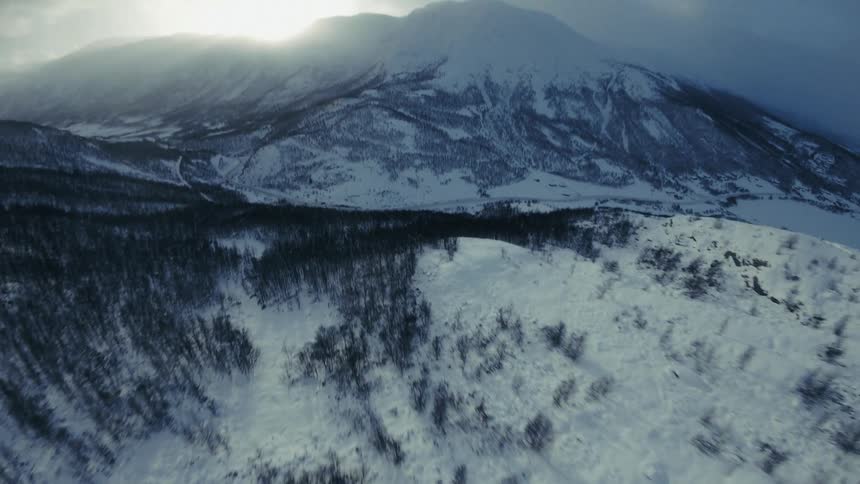 Snowcovered mountain landscape with the sun rising behind the peak under a cloudy sky