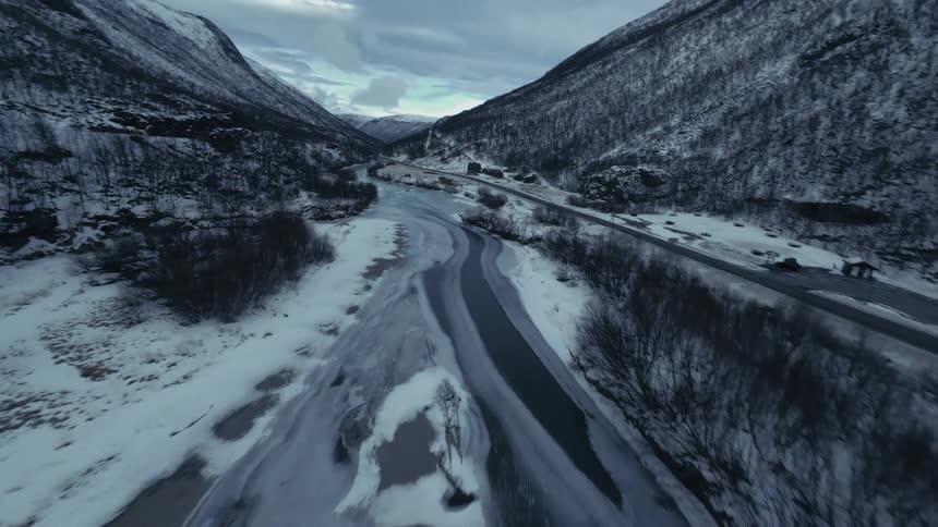 Winding river partially frozen in snowy mountain landscape