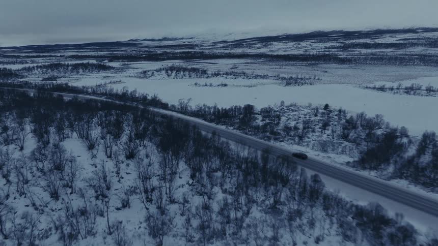 Two cars driving on a road surrounded by a vast snowcovered landscape under a cloudy sky