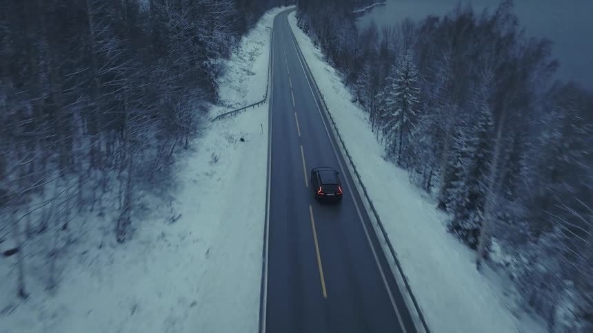 Van traveling on a forested mountain road along the coast under a cloudy winter sky