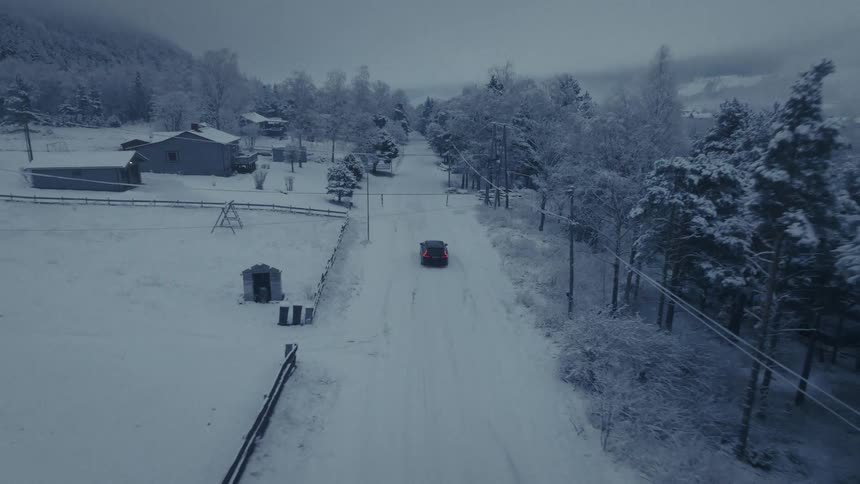 Car travels on a road in a snow covered forested mountain neighborhood under a cloudy winter sky