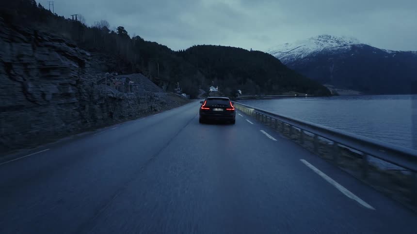 Automobiles travel on a road along the coast of a forested mountain river valley