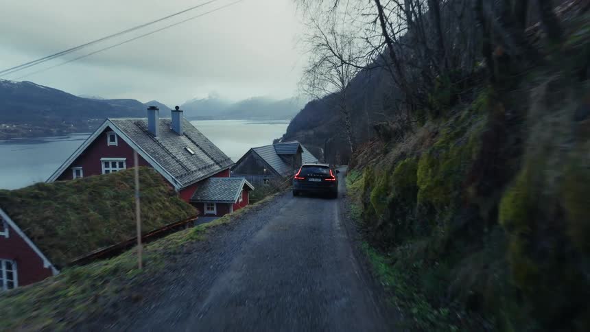 Automobile travels on a mountainside road overlooking houses on the coast