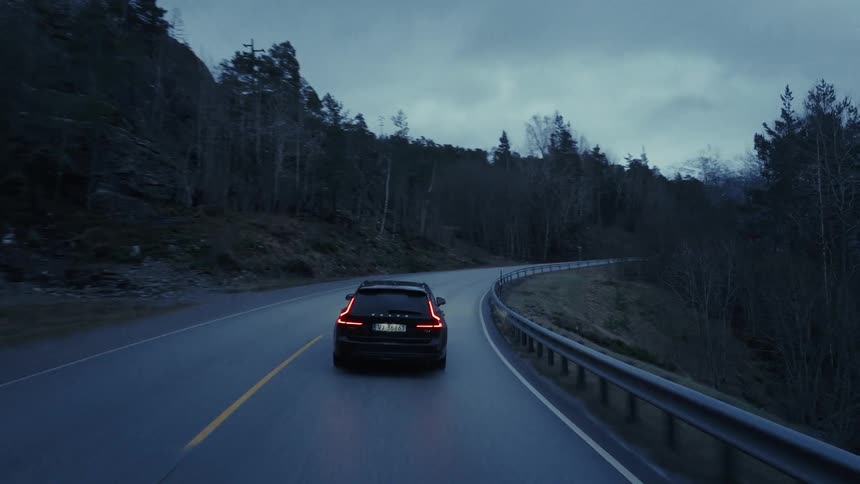 Automobile traveling on a forested mountain road under a cloudy sky