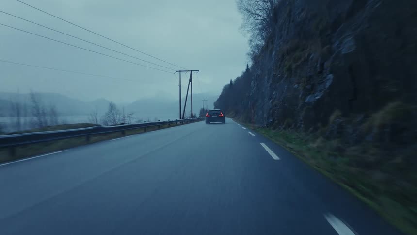 Automobile travels on a mountainside road overlooking the river and mountains in the distance