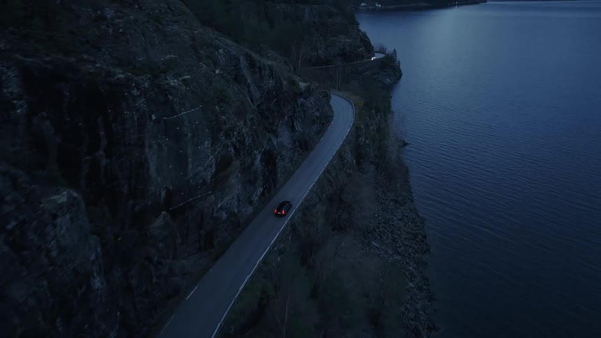 Automobiles travel on a road winding around mountains along the coast