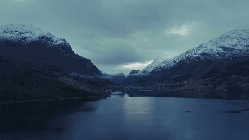 Snowcapped mountains surround a lake under cloudy sky