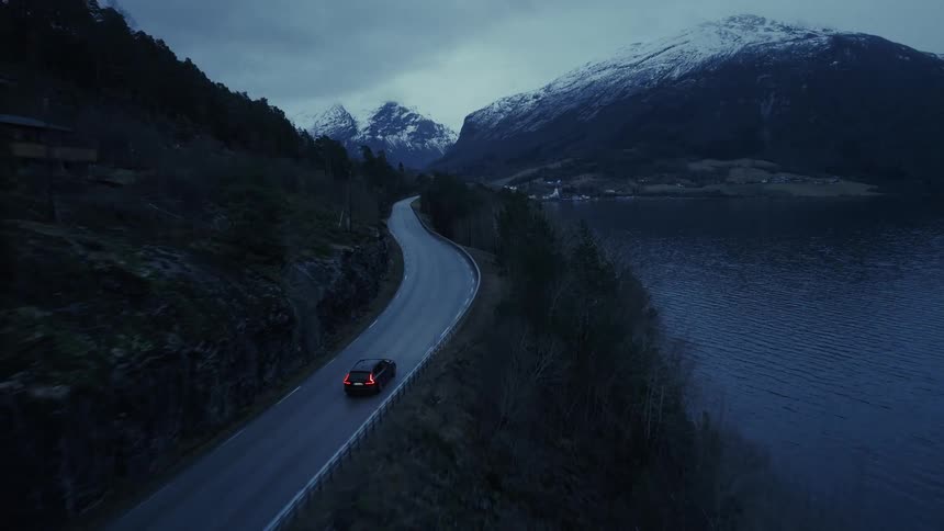 Car driving along a lakeside road between mountains with snowcapped peaks