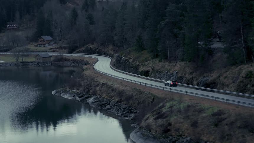 A car driving on a narrow road with a lake alongside it at midday