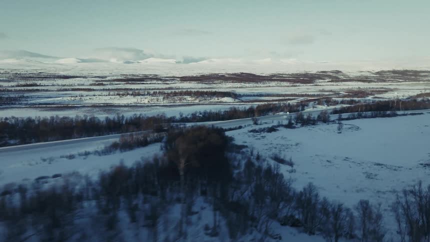 Car drives along road in vast snowy landscape with mountains in background