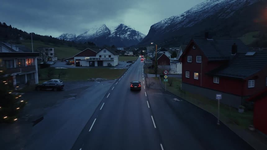 Cars travel on a road trough a mountaintop neighborhood with mountains in the distance