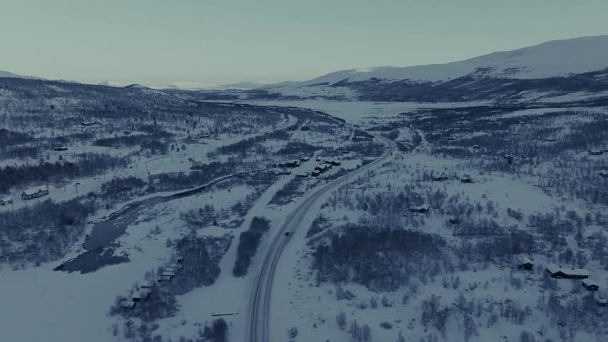 Automobile travels on a freeway through snow covered woodland and mountains