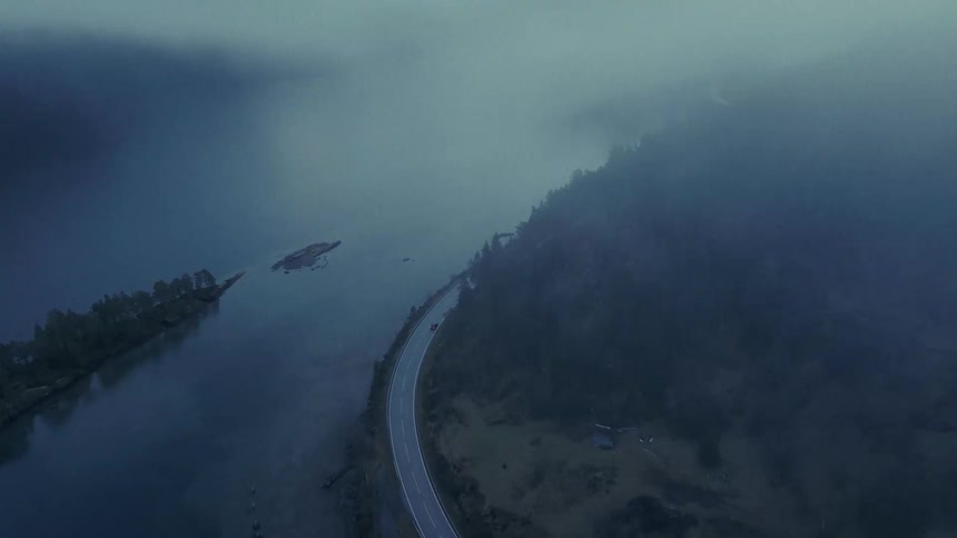 Car traveling on a road around a forested mountain along the coast under a cloudy sky