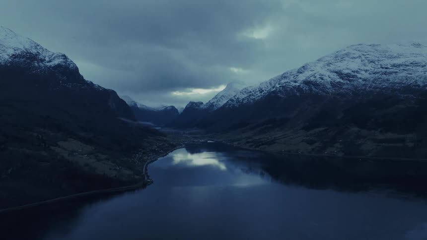 Snowcovered mountains reflected in lake under cloudy sky