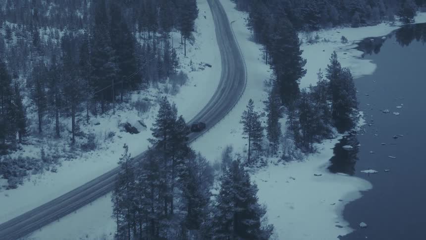 Automobile traveling on a forested mountain road around a curve overlooking the coast