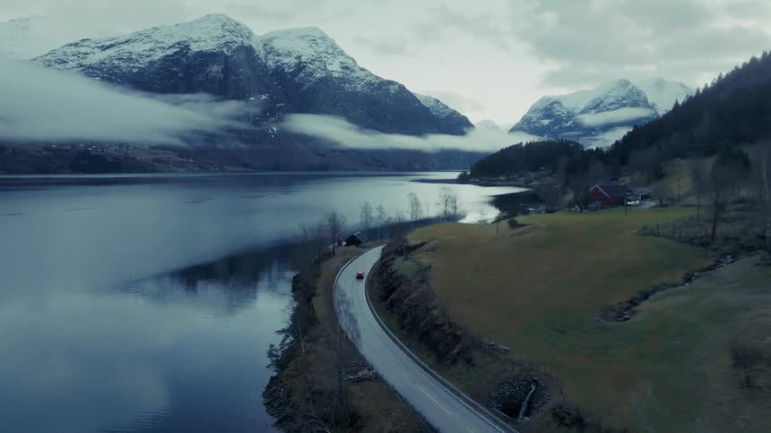 Car driving along a lakeside road with snowcovered mountains in the background